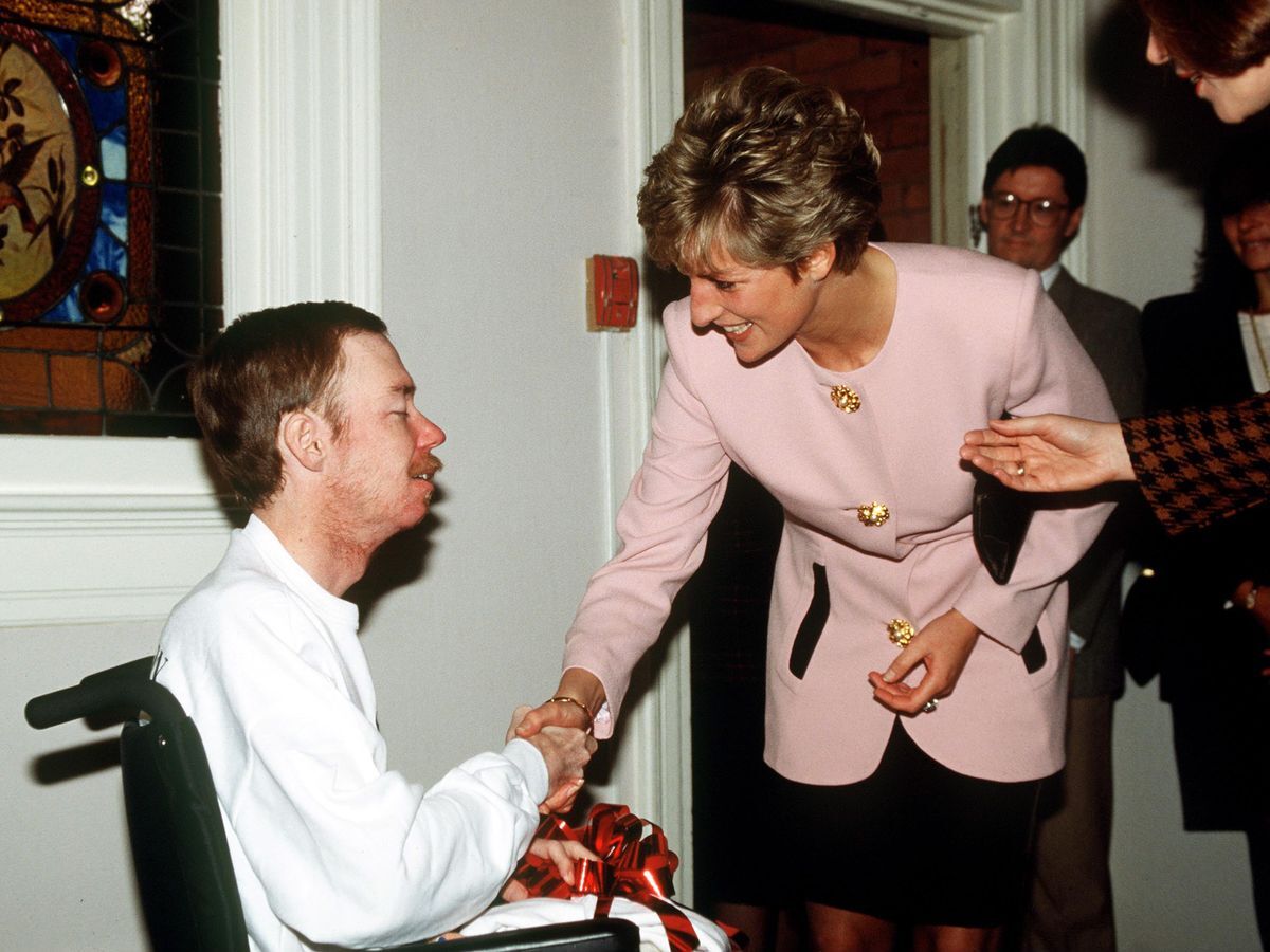 Princess Diana shaking hands with a patient at a London hospital, circa 1980s. She is smiling warmly and wearing a casual outfit.